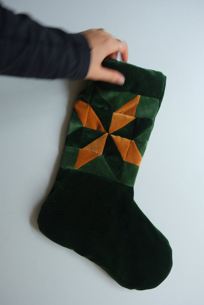 Green and orange star-patterned stocking held by a hand on a white background